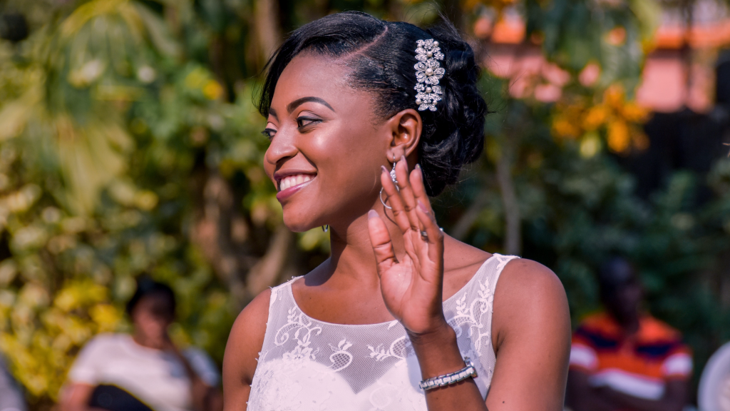 Noiva de pele negra e cabelo preso acenando sorrindo para os convidados no casamento