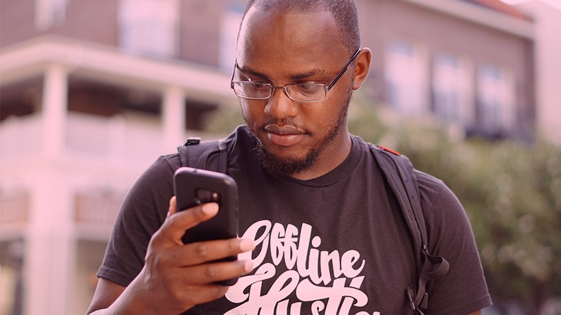 homem negro de óculos e barba olhando o celular com camiseta preta