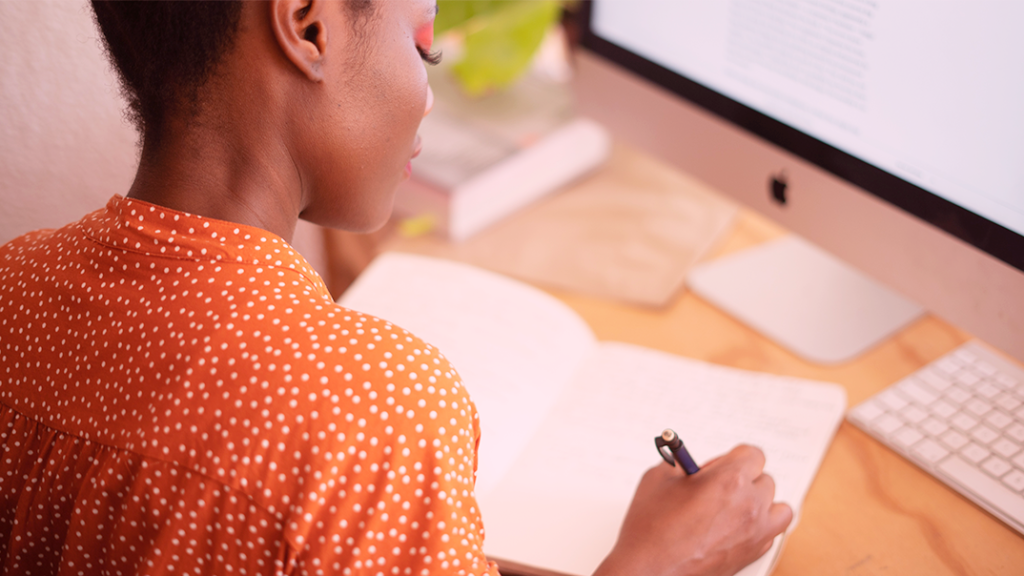 Mulher negra escrevendo num caderno. Pegar um empréstimo para abrir um negócio envolve certo planejamento. Veja como estruturar esse processo em poucos passos.