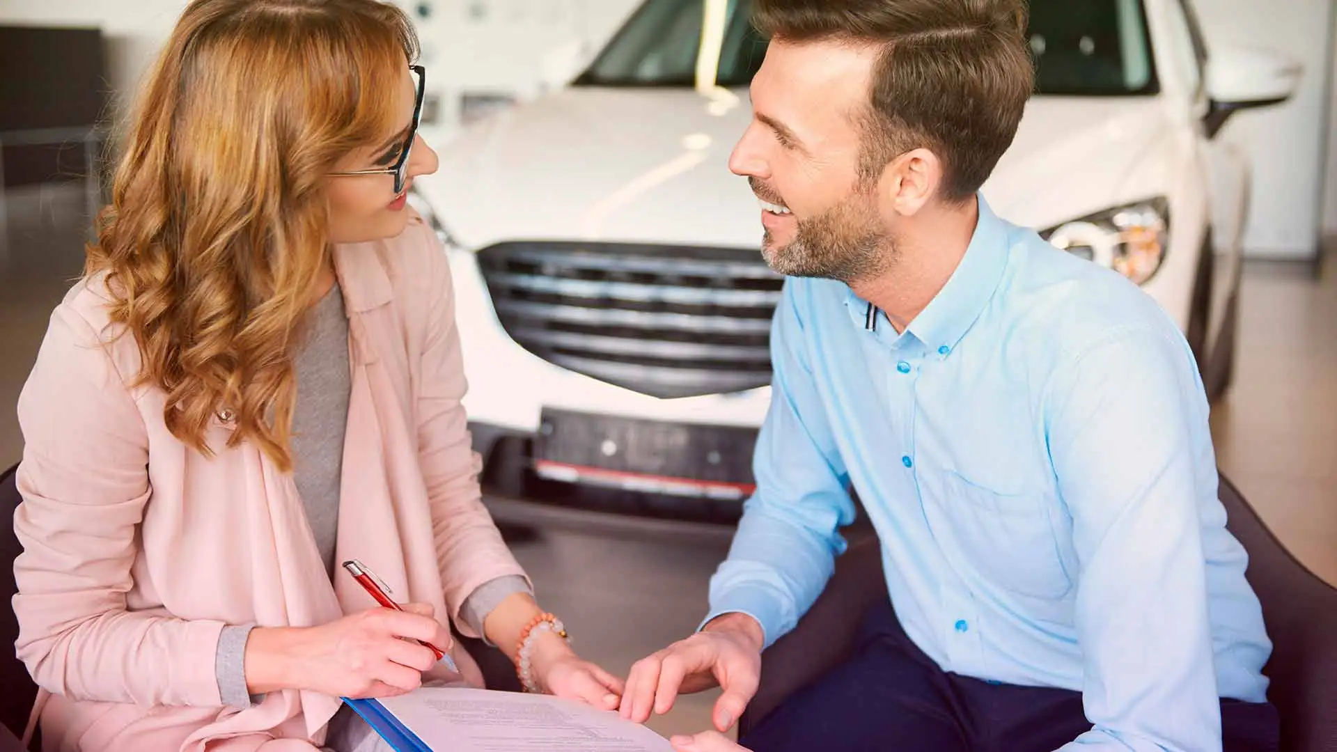 Descubra: Financiamento de veículos - juros, prazo, documentos e vantagensum homem e uma mulher conversando e anotando na frente de um carro